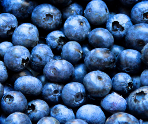 "Close-up of tightly packed fresh blueberries in varying shades of blue and purple, with a frosted skin texture and small indentations at the top of each berry."
